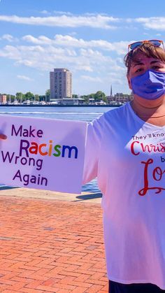 a woman wearing a face mask holding up a sign that says make racism wrong again