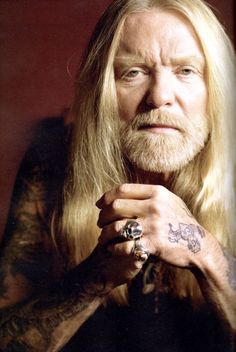 a man with long blonde hair and tattoos on his arm, looking at the camera