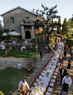 a long table is set up outside in front of an old house with people walking around it