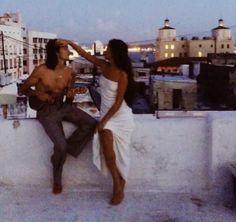 a man and woman sitting on top of a building next to each other