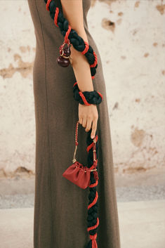 a woman in a long dress holding a red and black handbag with a bell on it