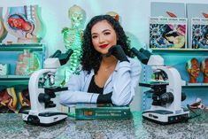 a woman standing in front of two microscopes with her hands on the top of them