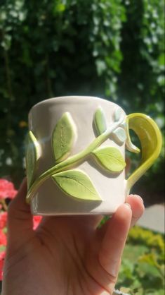 a hand holding a white coffee cup with green leaves on it