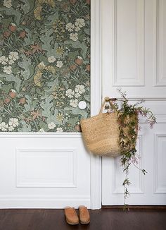 a wall with flowers and plants on it next to a purse hanging up against the wall