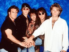 a group of people standing next to each other in front of a blue background holding hands