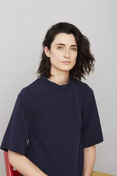 a woman sitting in a red chair with her hands on her hips and looking at the camera