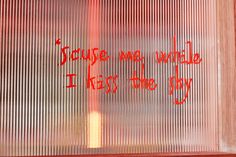 graffiti written on the side of a window in front of a red wall with words