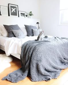 a cat sitting on the edge of a bed next to pillows and blankets in a bedroom