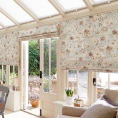 a living room filled with furniture and windows covered in roman blind shades on top of them