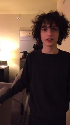 a young man with curly hair standing in a living room