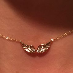 a close up of a person wearing a gold necklace with wings on the back of their neck