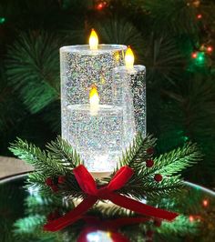 two lit candles sitting on top of a table next to a christmas wreath and tree