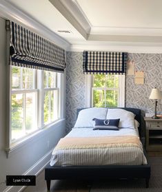 a bed sitting in a bedroom next to two windows with roman shades on the window sill