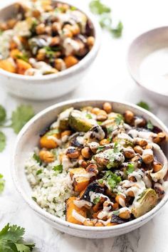 two bowls filled with rice and vegetables on top of a white counter next to sauce