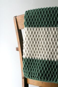 a green and white crocheted blanket sitting on top of a wooden chair