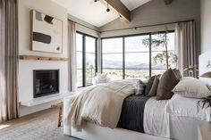 a bedroom with a large bed and a fireplace in the corner near two windows that look out onto mountains