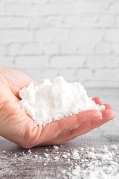 a hand holding some white powder in front of a brick wall