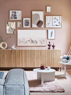 a living room with pink walls and pictures on the wall above the coffee table in front of the couch