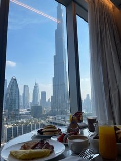 a table with plates of food and drinks in front of a window overlooking the city