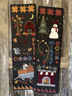 two quilted wall hangings with snowmen and houses in them on a wooden background