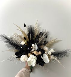 a hand holding a bouquet of flowers on a white wall with black and gold feathers