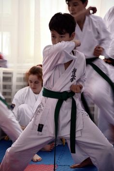 two young boys are practicing karate moves while another boy watches from the sidelines in front of them