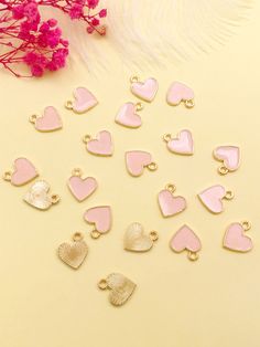 pink and gold heart shaped charms on a table next to feathers, flowers and beads