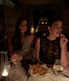 two women sitting at a table with food and drinks