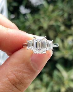 a person holding an engagement ring with three stones on the side and one stone in the middle