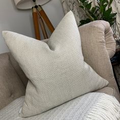 a white pillow sitting on top of a gray couch next to a lamp and plant