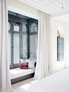 a white bed sitting next to a window covered in curtains