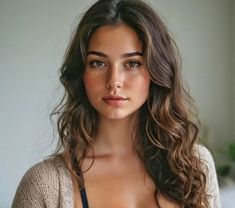 a beautiful young woman with long brown hair wearing a black bra and tan cardigan