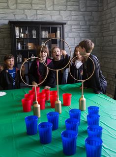 a group of people standing around a green table with cups on it and an object in the middle