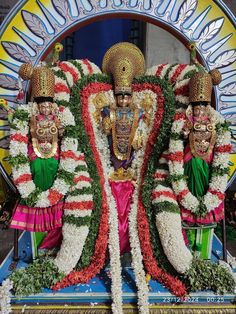 two men dressed in elaborately decorated costumes standing next to each other with flowers all around them