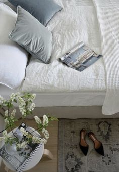 a bed with white linens and pillows next to a table with flowers on it