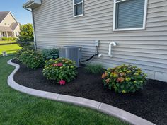 an air conditioner sitting on the side of a house next to flowers and bushes