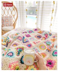 a person is holding a coffee cup in front of a crocheted blanket