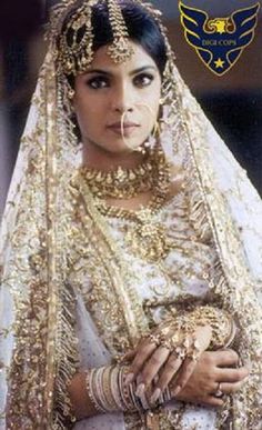 a woman wearing a gold and white bridal outfit with her hands on her chest