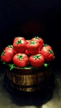 a bunch of red tomatoes sitting on top of a wooden barrel filled with green leaves