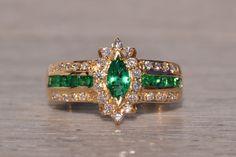 two gold rings with green and white stones on each ring, one has a pear shaped emerald surrounded by smaller diamonds