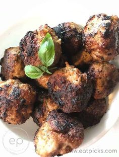 some meatballs on a white plate with a leafy green sprig in the middle