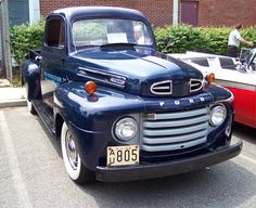 an old blue truck parked next to another red car