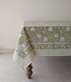 a green and white table cloth with flowers on it is sitting on a wooden stand