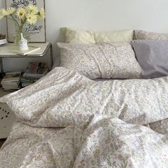 an unmade bed with white sheets and flowers in a vase on the end table