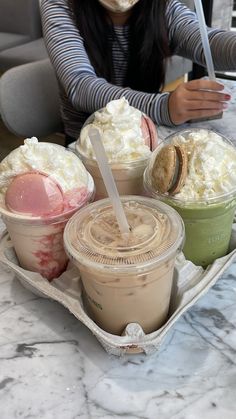 a woman sitting at a table with three cups of ice cream and two desserts