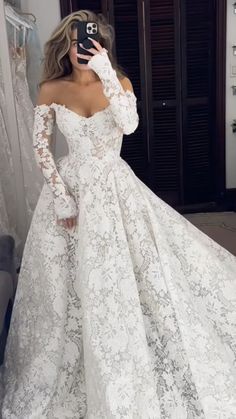 a woman taking a selfie wearing a wedding dress with long sleeves and an off the shoulder lace top