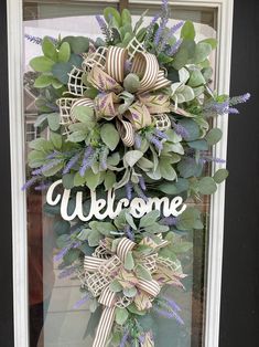 a welcome sign hanging on the front door with purple flowers and greenery around it