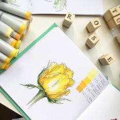 a yellow rose sits on top of some colored crayons and scrabbles