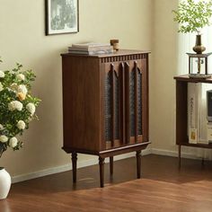 a wooden cabinet sitting in the corner of a room next to a vase with flowers