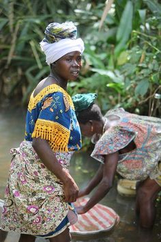 two women are washing their feet in the water while another woman stands near them and smiles